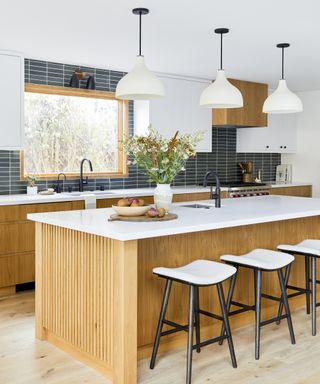 A kitchen with white oak cabinets and a white quartz-topped island with black and white bar stools