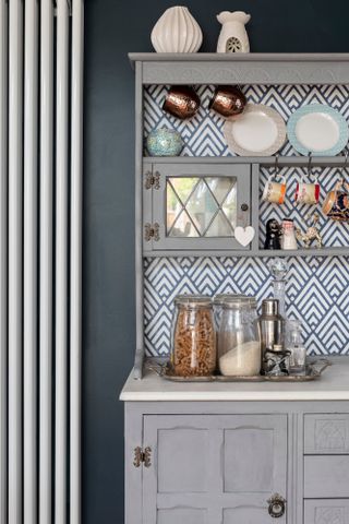Close-up of kitchen dresser with grey painted front and blue and white geometric papered back