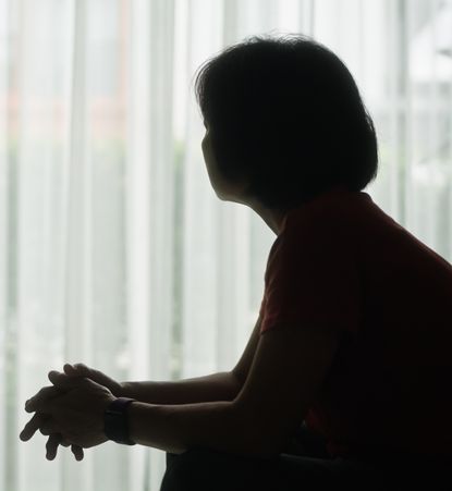 A silhouette of a woman sitting down and looking toward a window.