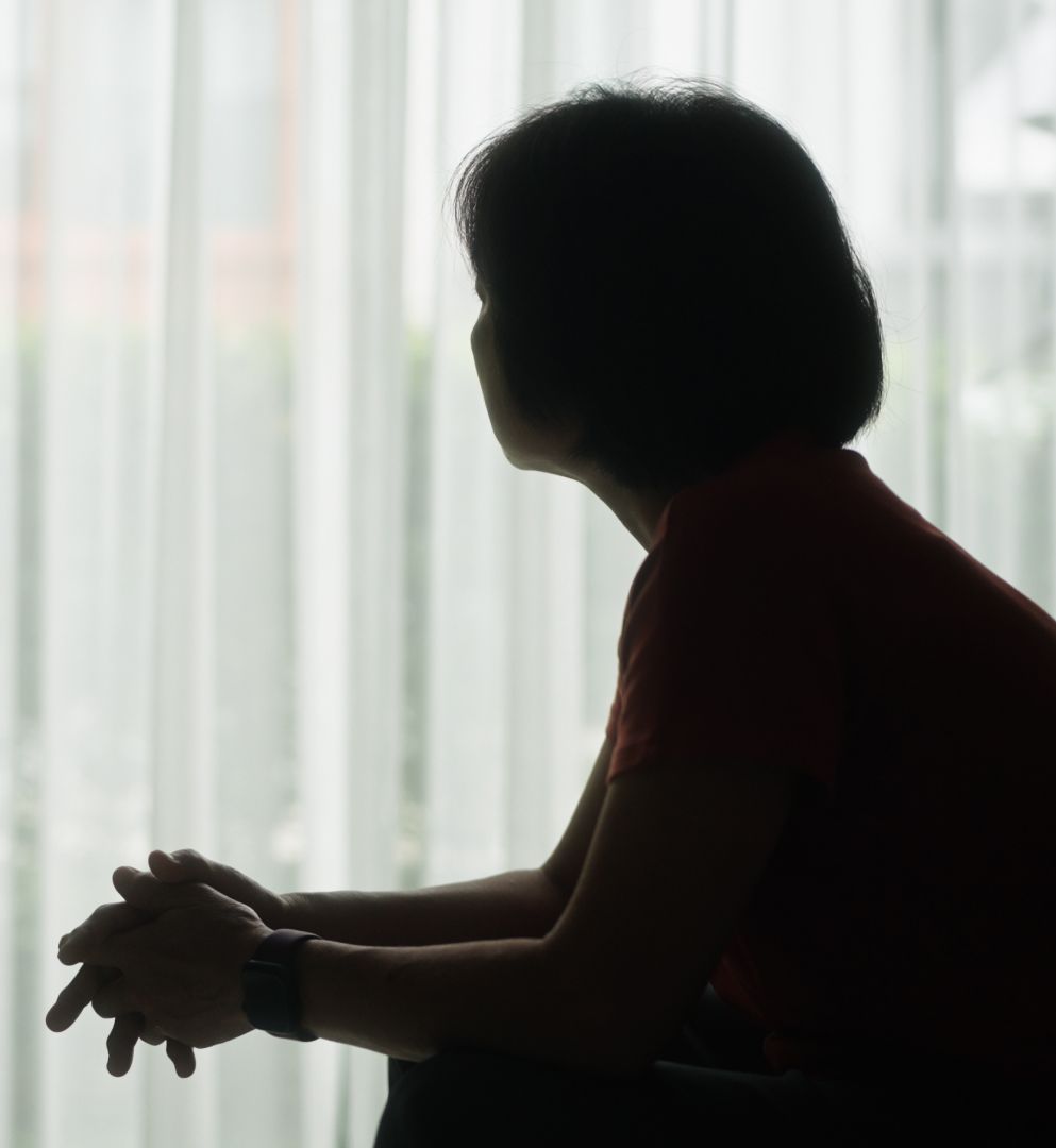 A silhouette of a woman sitting down and looking toward a window.