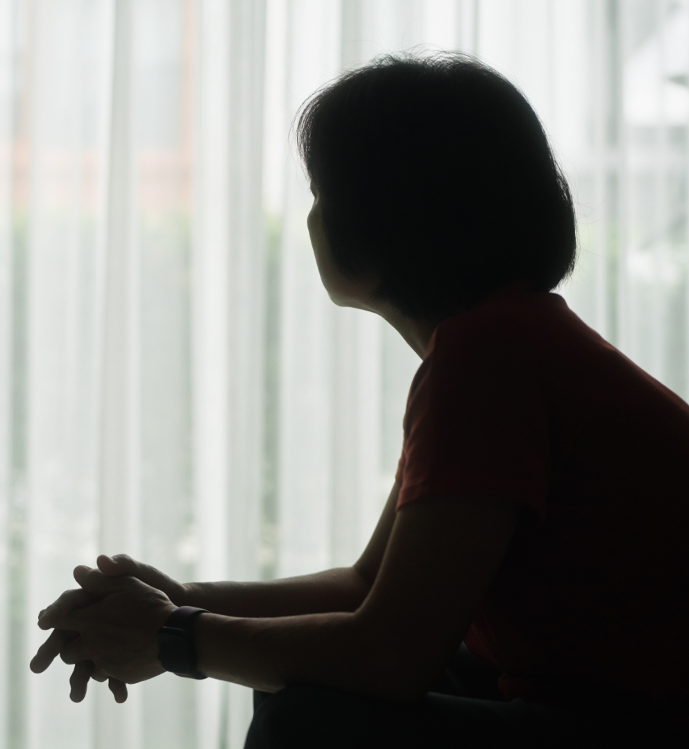 A silhouette of a woman sitting down and looking toward a window.