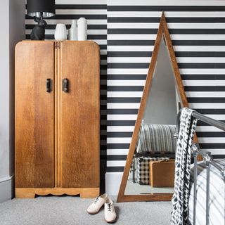 bedroom with white and black strip wallpaper wooden cupboard and triangular mirror