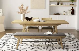 Modern dining room with wooden dining table, matching bench with seat cushion and matching chairs, geometric rug