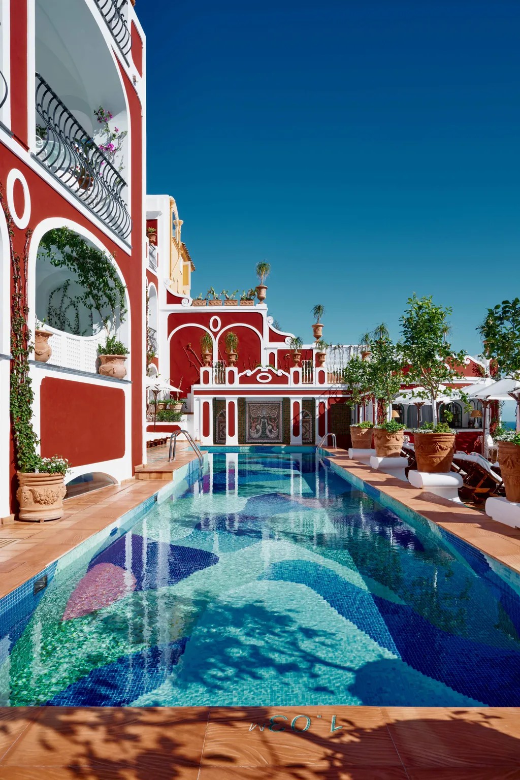 Aerial views of a colorful, vibrant pool with a bed made up of tiled waves in tones ranging from dark blue to green.
