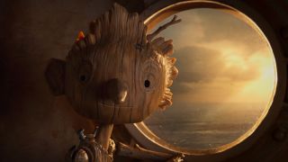 Pinocchio stands smiling next to a ship's window in Guillermo del Toro's Pinocchio.