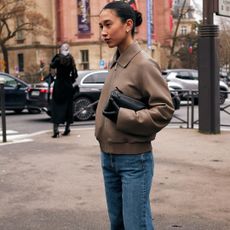 Fashion week attendee wears brown leather jacket, jeans and slicked bun hair