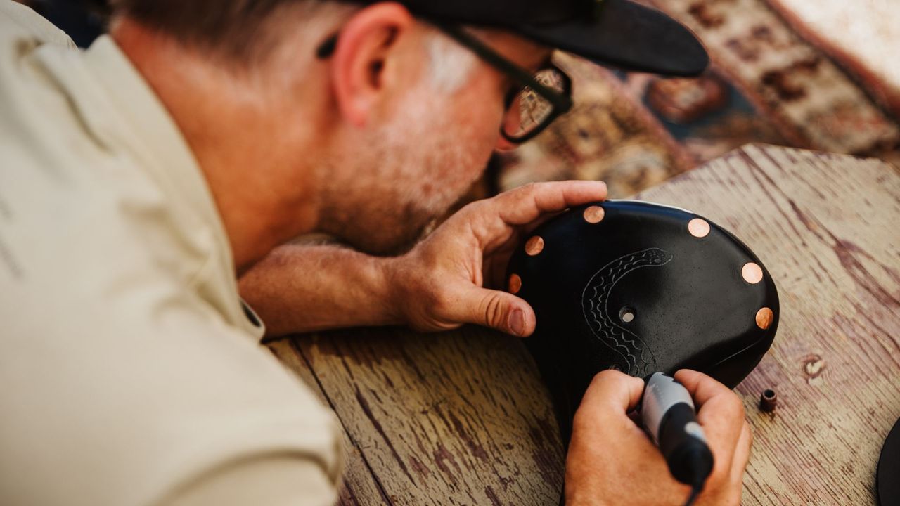 Image shows artist Jeremy Collins etching a design onto a Brooks B17 saddle