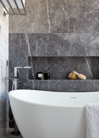 A bathroom with a white curved bath and grey marble walls