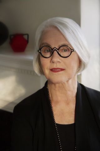 a photo of an older woman with short white hair, wearing black rimmed glasses and a black coat and shirt