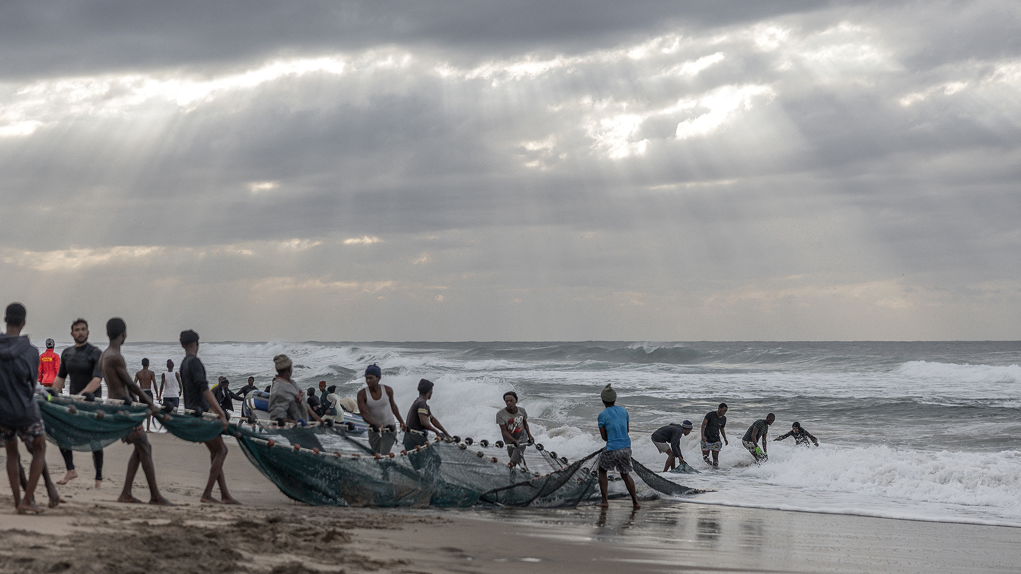 A group of fishermen drag an enormous sardine net onto Scottburgh beach near Durban, South Africa