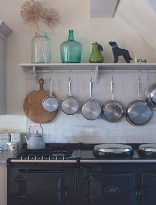kitchen with white wall tiles, a grey shelf with silver pans hanging from, a black stove and black aga