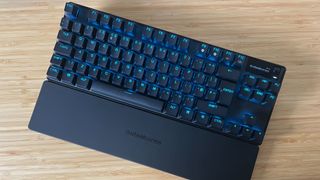 SteelSeries Apex Pro TKL Wireless gaming keyboard with wrist rest on a wooden desk