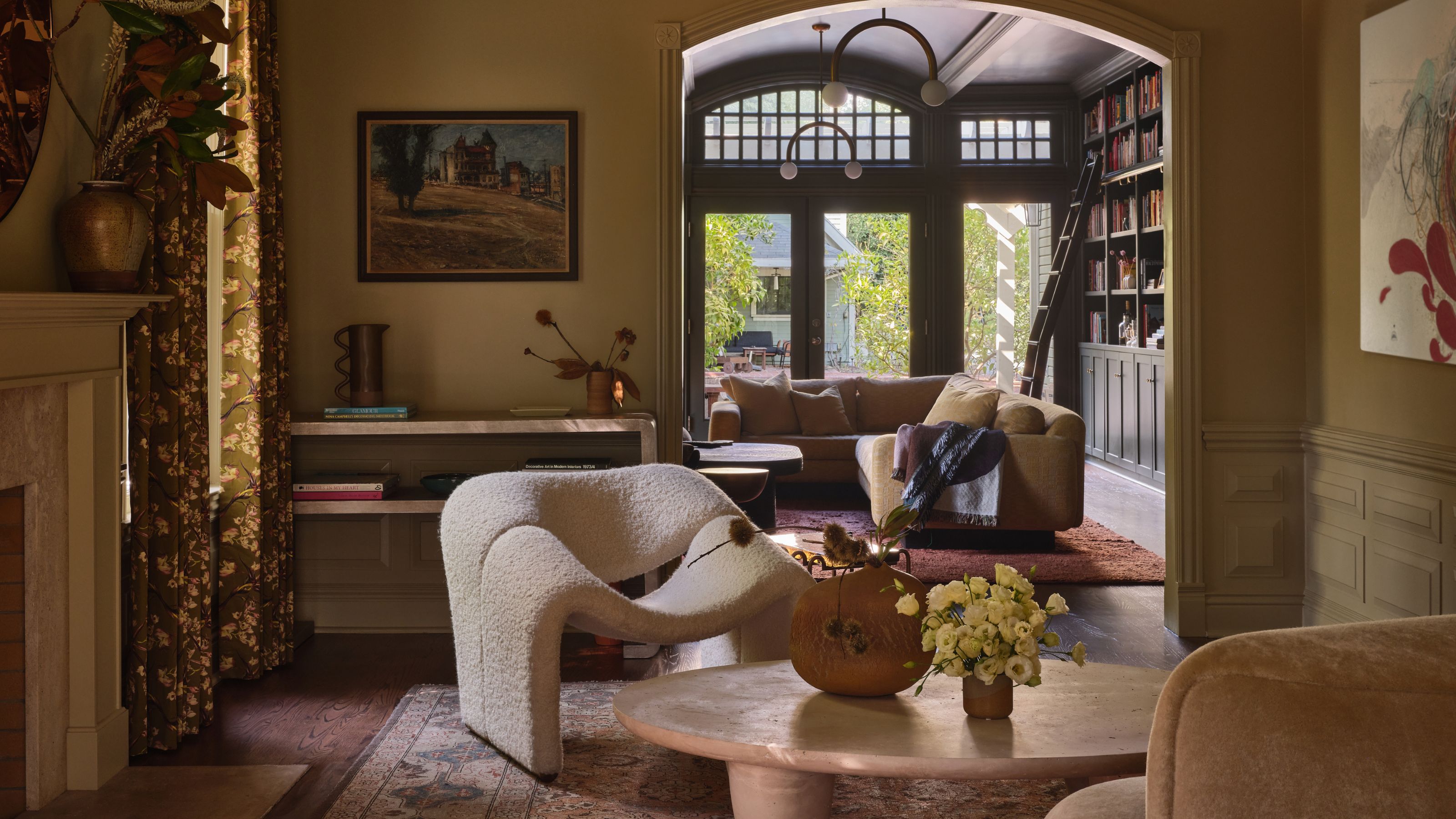 a soft yellow Victorian living room with bold modern decor looking through to a rich green garden room