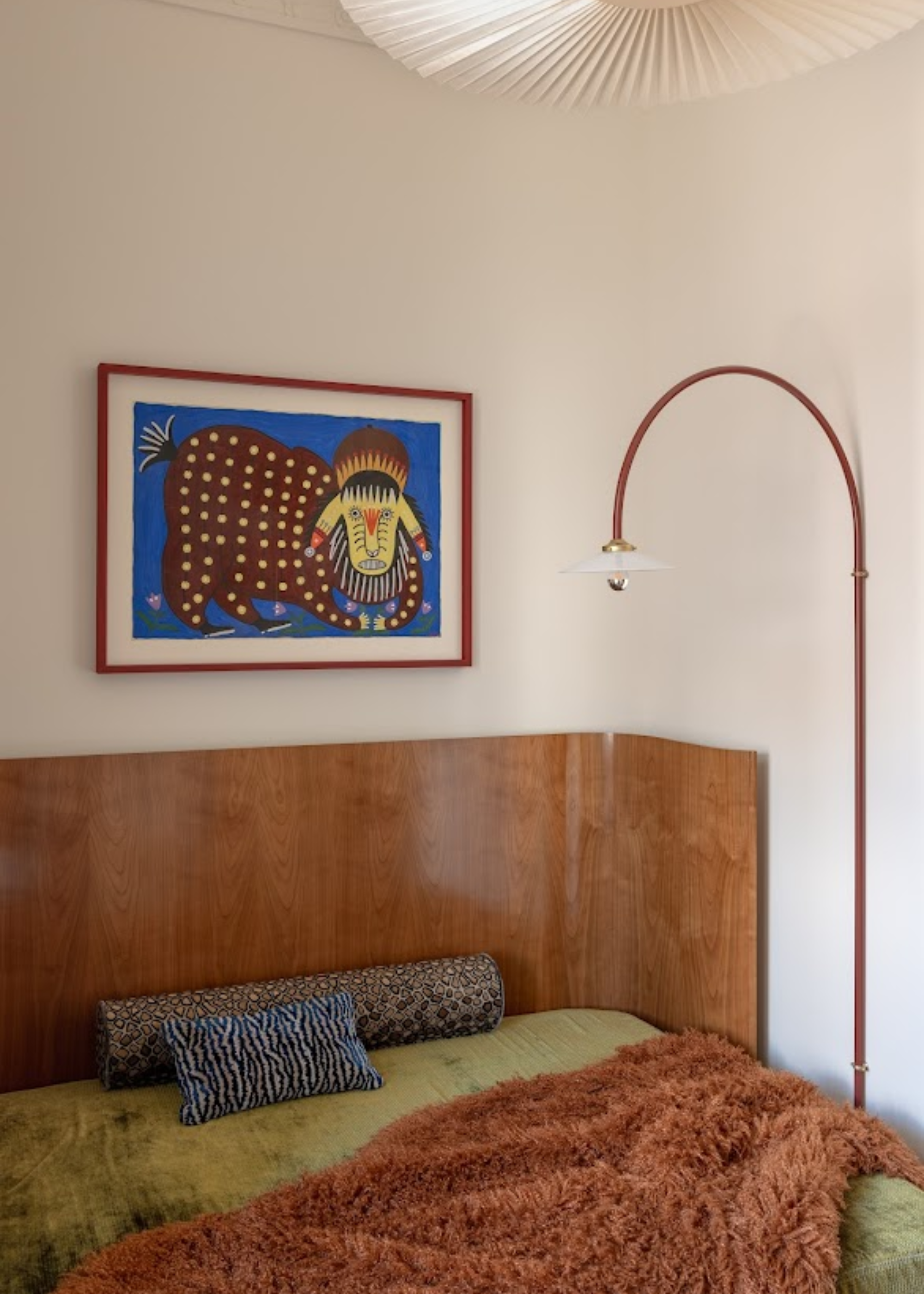 A small bedroom with an oversized wood headboard, a framed painting above the bed, a curved floor lamp, a pleated pendant, a brown fuzzy throw, a bolster pillow and an animal print pillow