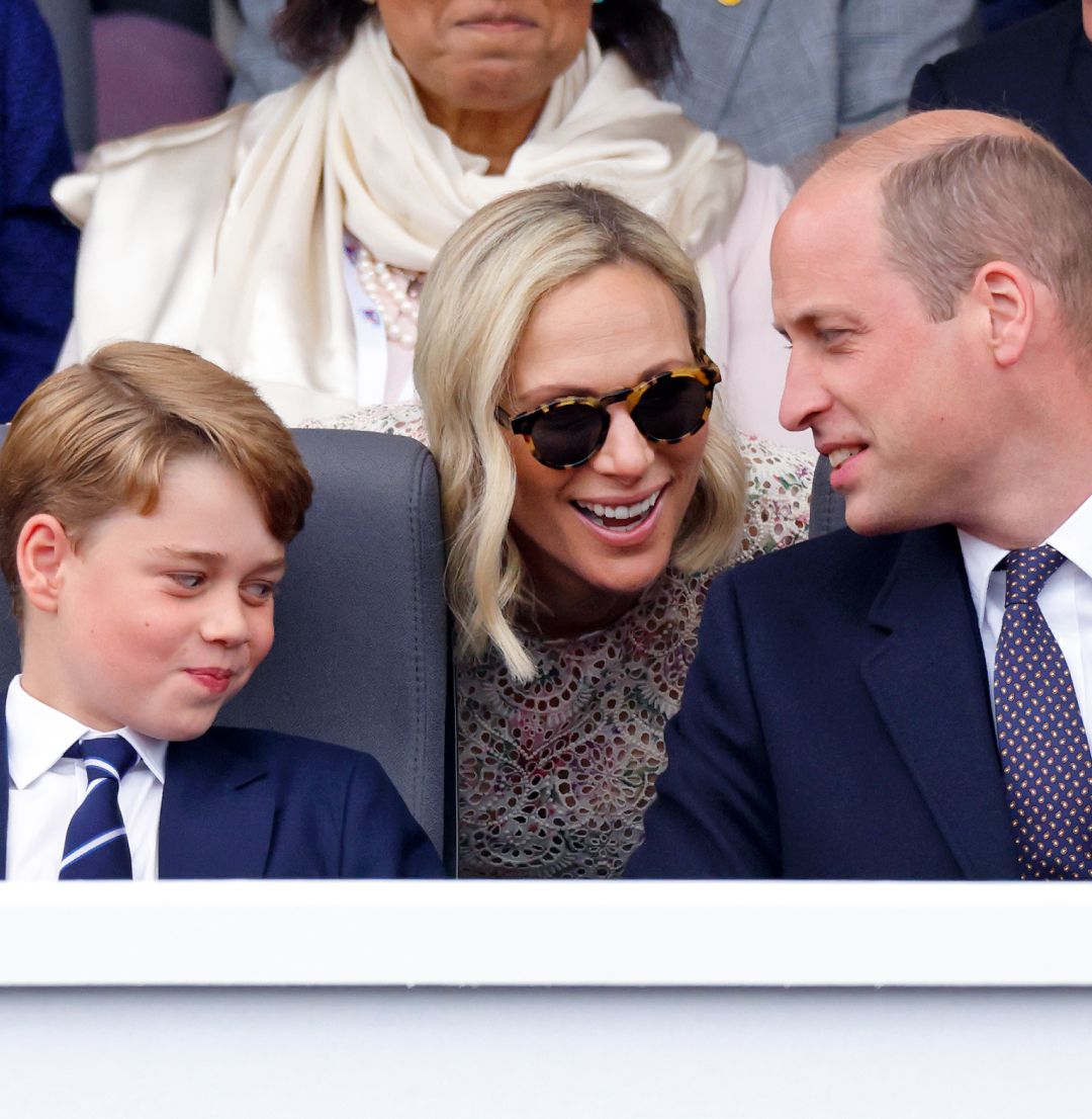 Prince George smirking as Zara Tindall leans over and talks to Prince William