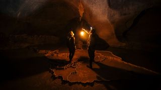 Woman standing in cave with man lit by lantern