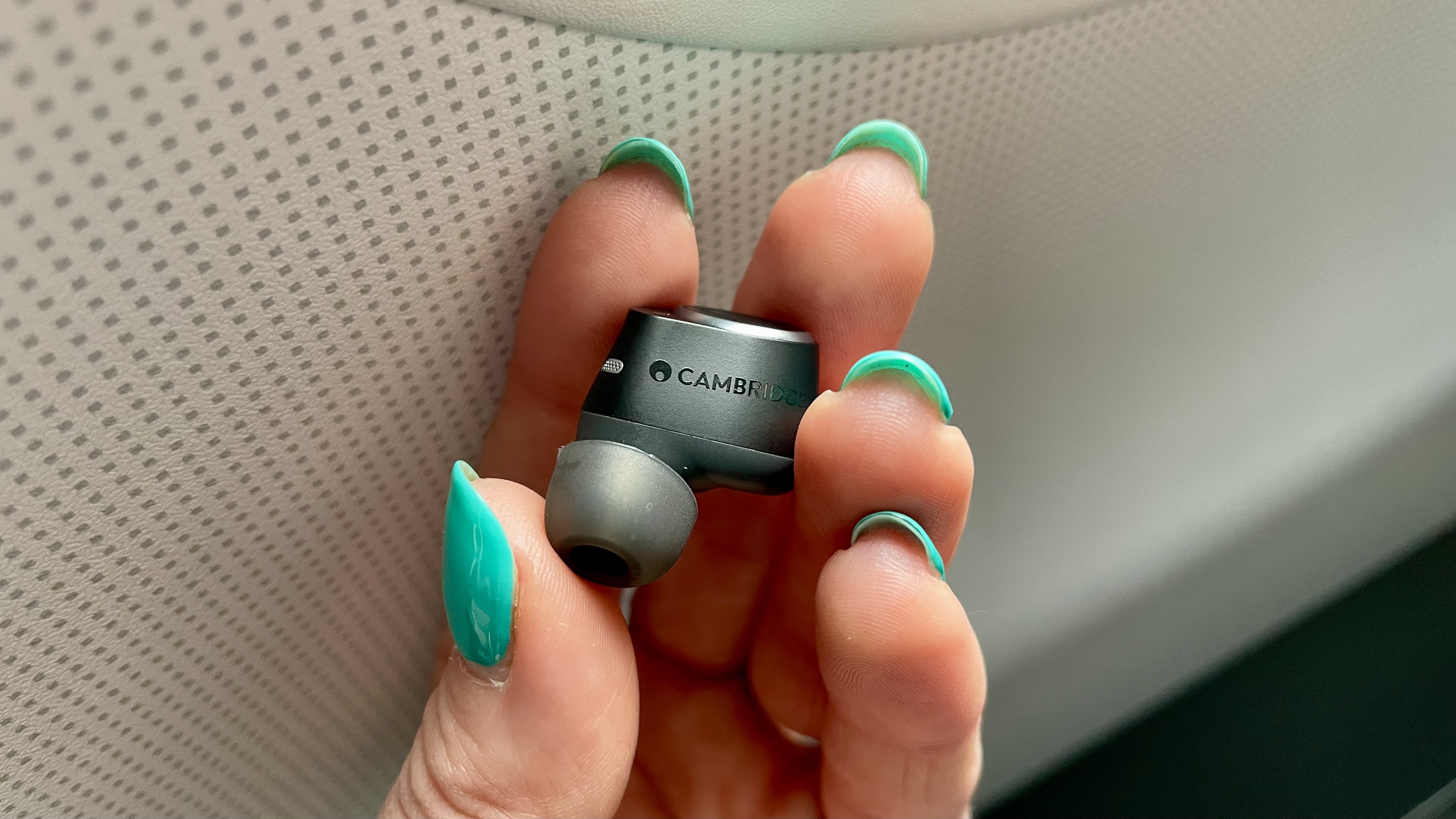 Cambridge Audio Melomania M100 one earbud, held in a hand