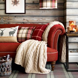 A cosy living room with wood cladding on the walls and a red sofa with chunky knit throw