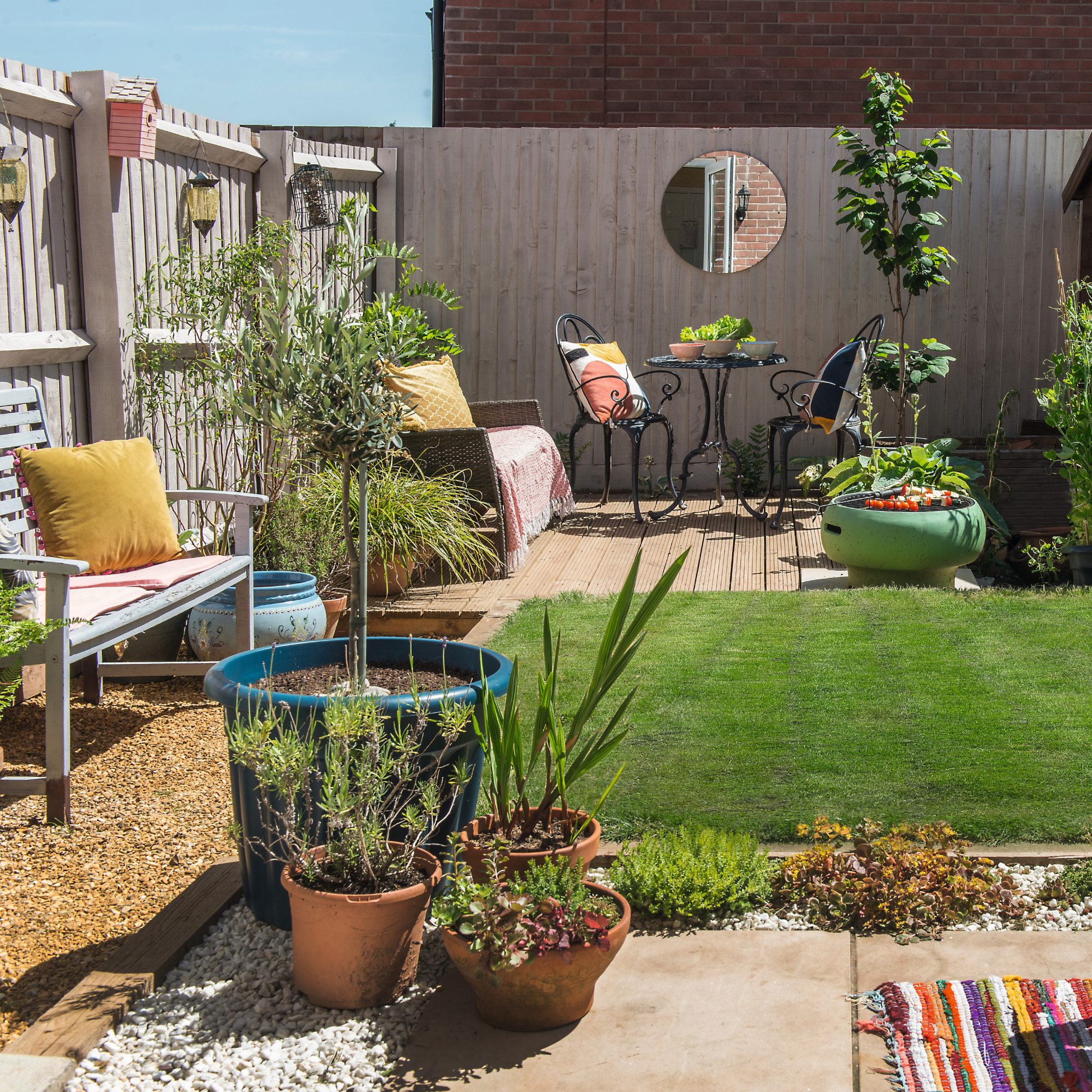 Sunny garden with terracotta pots, pastel furnishings and black iron garden furniture.