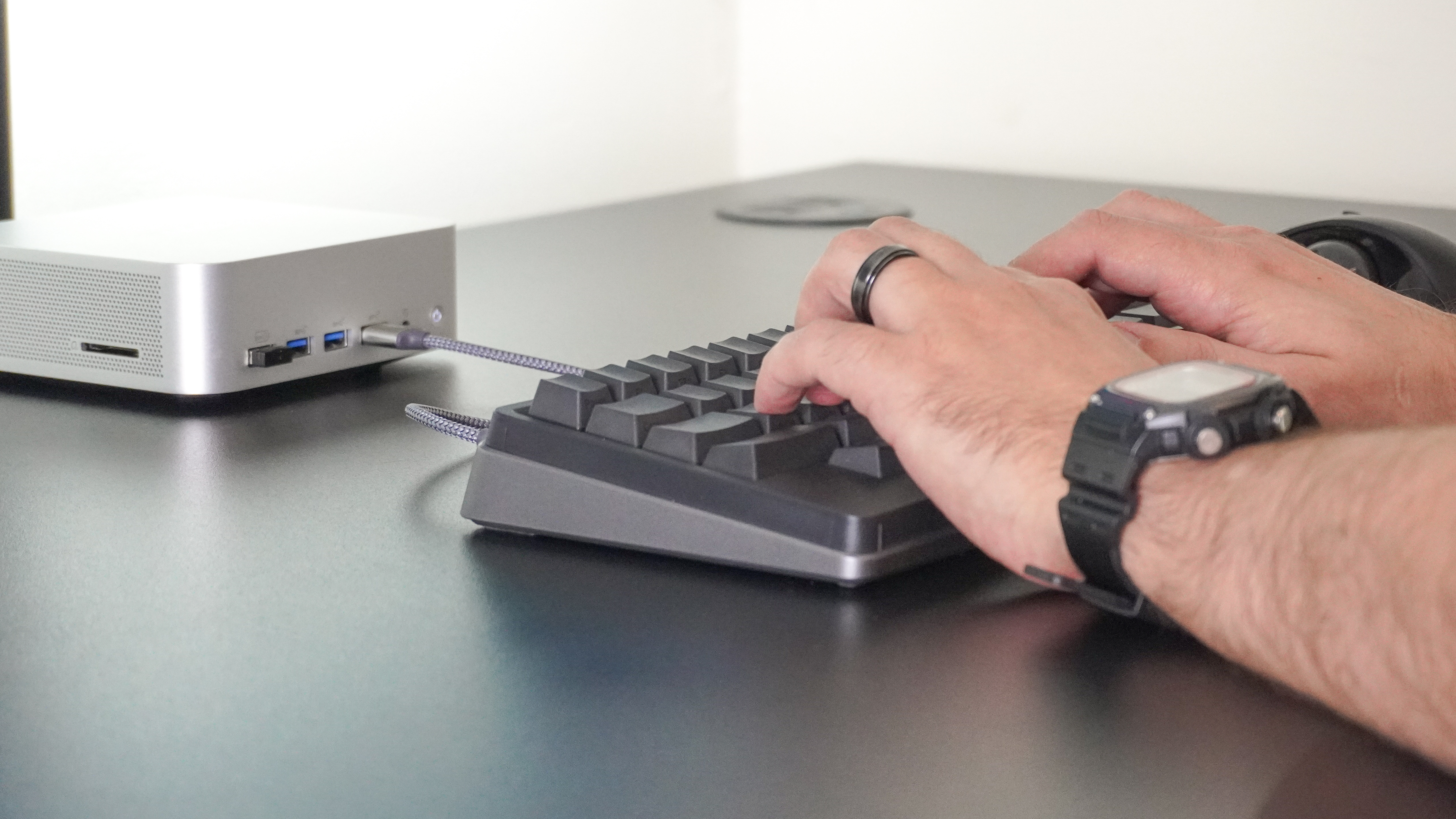 A person typing on the HHKB Studio keyboard with a mini PC in the background