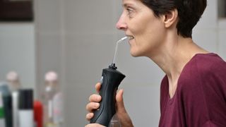 middle-aged woman using a black water flosser in her bathroom