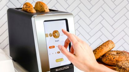 Revolution InstaGLO Toaster on countertop with bagels inside the toaster and surrounding on the countertop