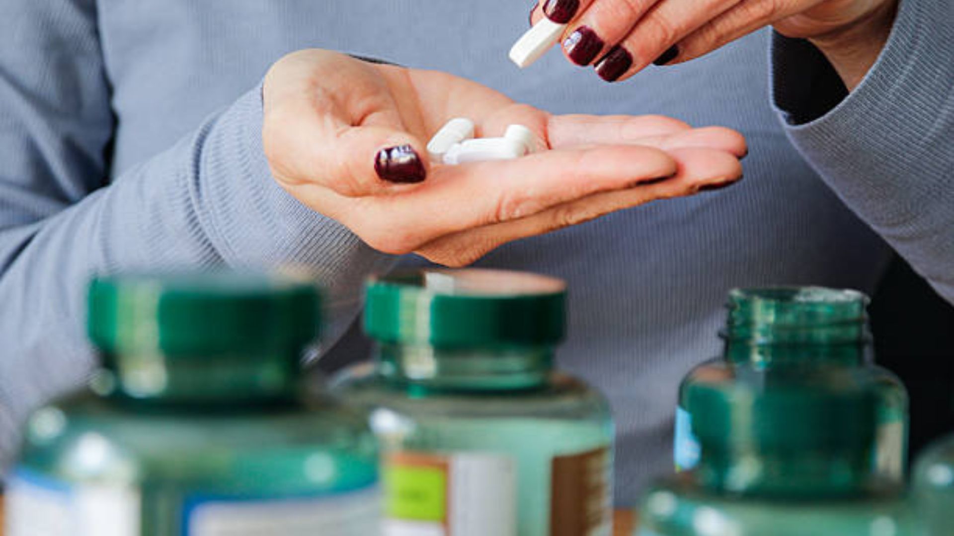 A woman&#039;s manicured hand holds a handful of white multivitamin supplements.