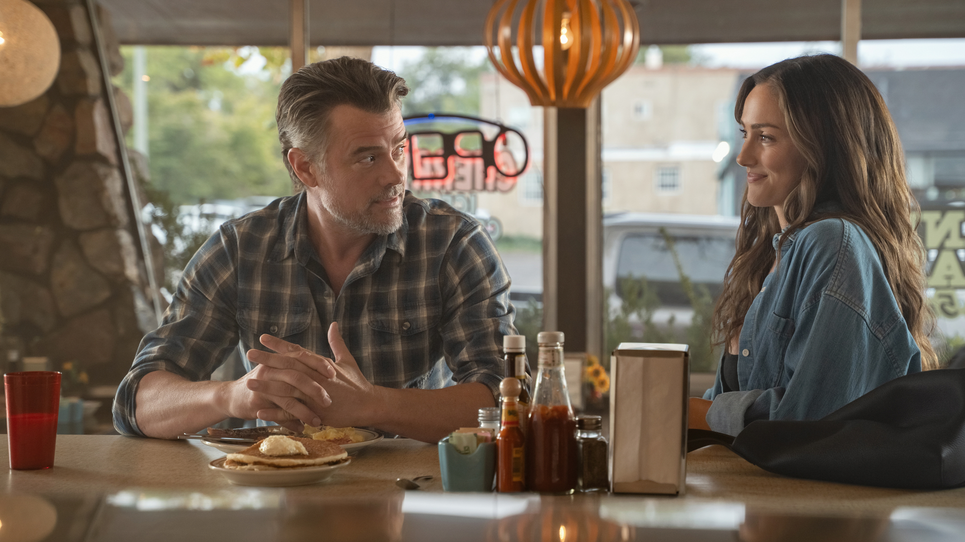 Josh Duhamel as Staten and Minka Kelly as Quinn look at each other while sitting at a diner counter in Episode 203 of 'Ransom Canyon' Season 2.