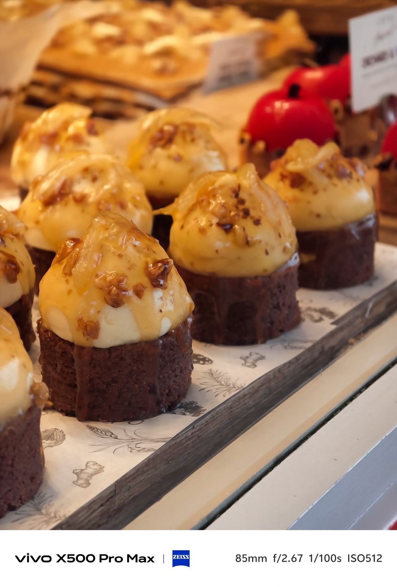 Display of chocolate cakes topped with cream and chopped nuts in a warmly lit bakery window.