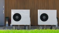 two heat pumps outside house with timber clad wall and grey door