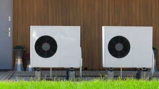 two heat pumps outside house with timber clad wall and grey door