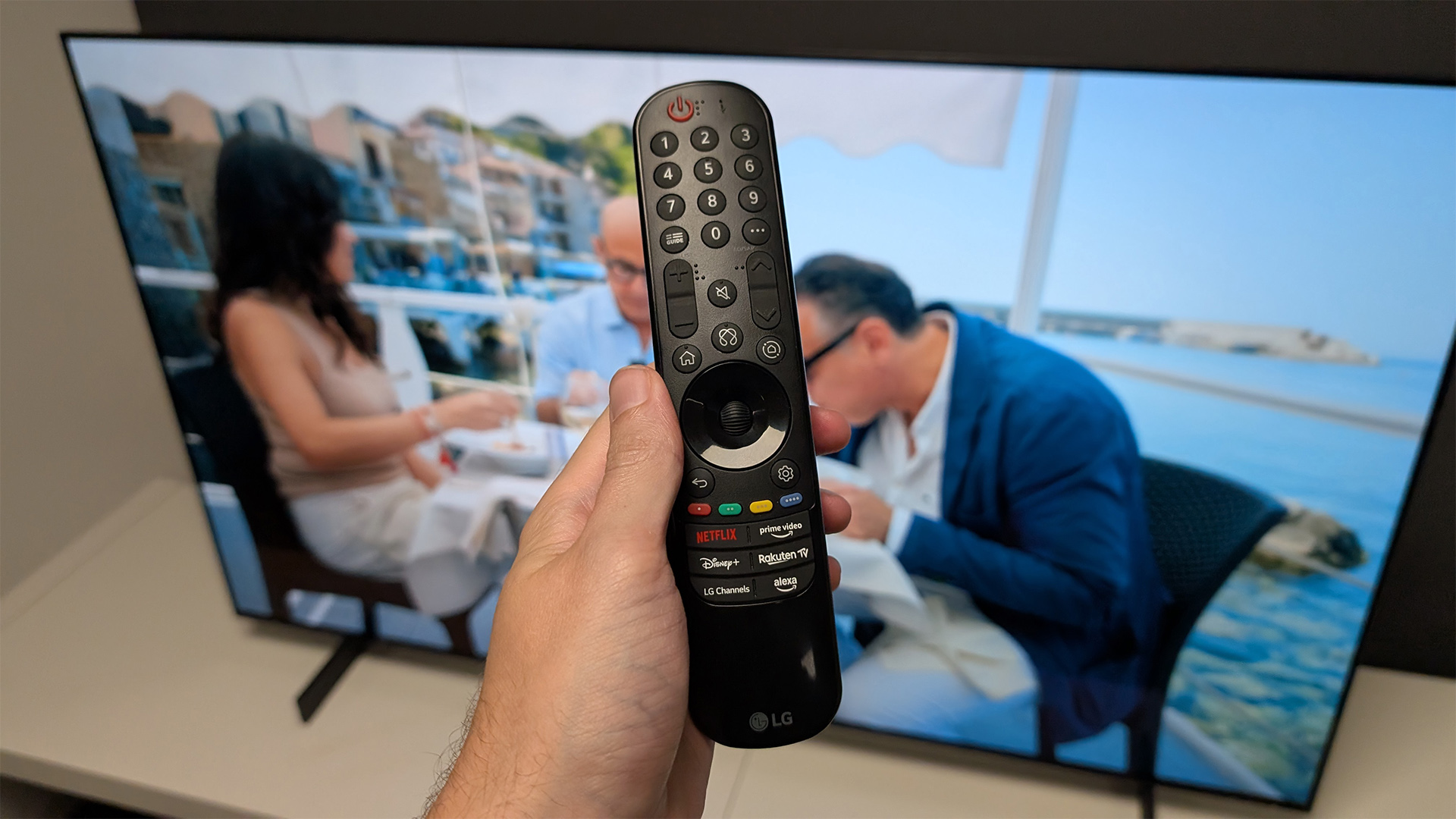 LG C5 42-inch OLED TV remote held in hand in front of TV