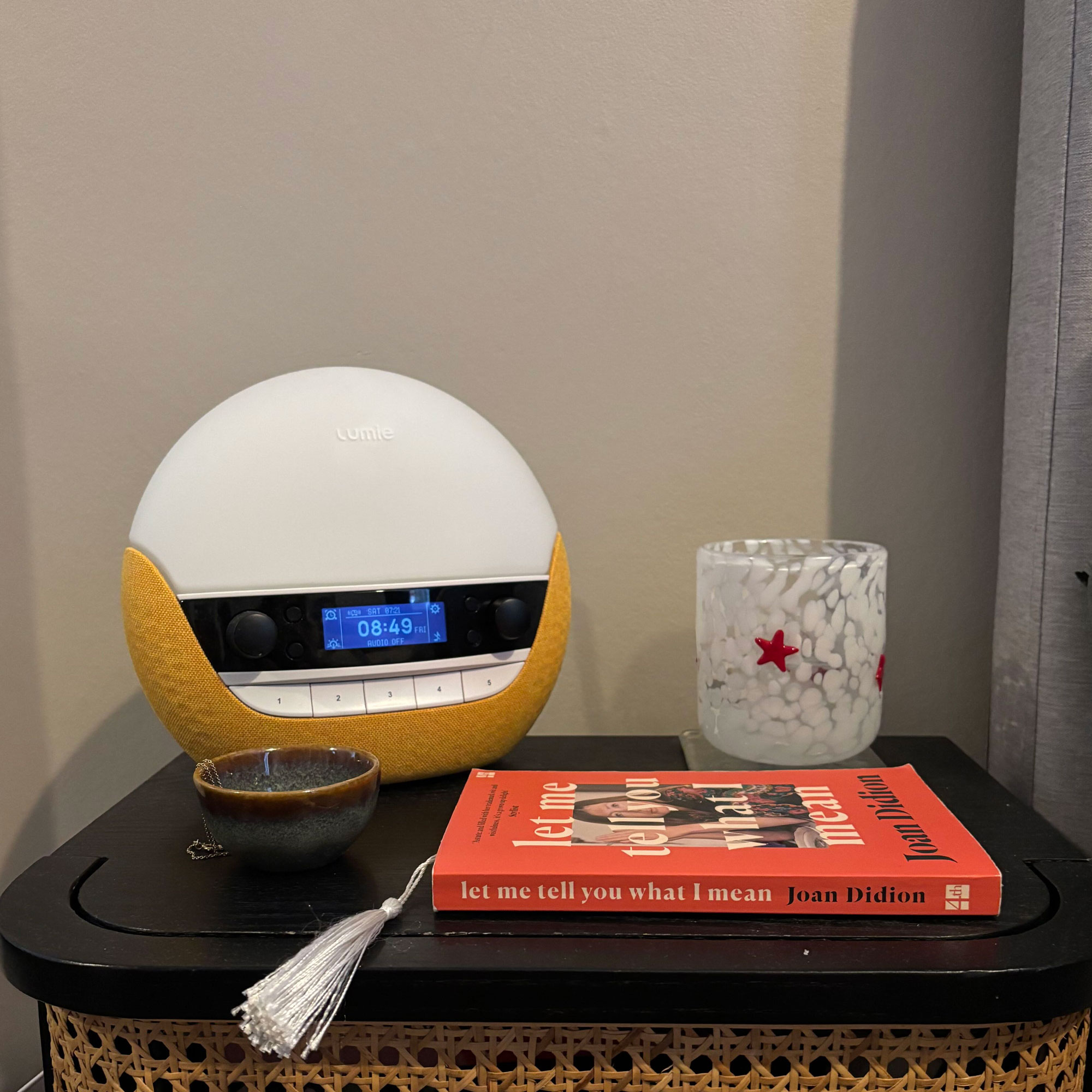 Yellow sunrise alarm clock on black bedside table with a red book