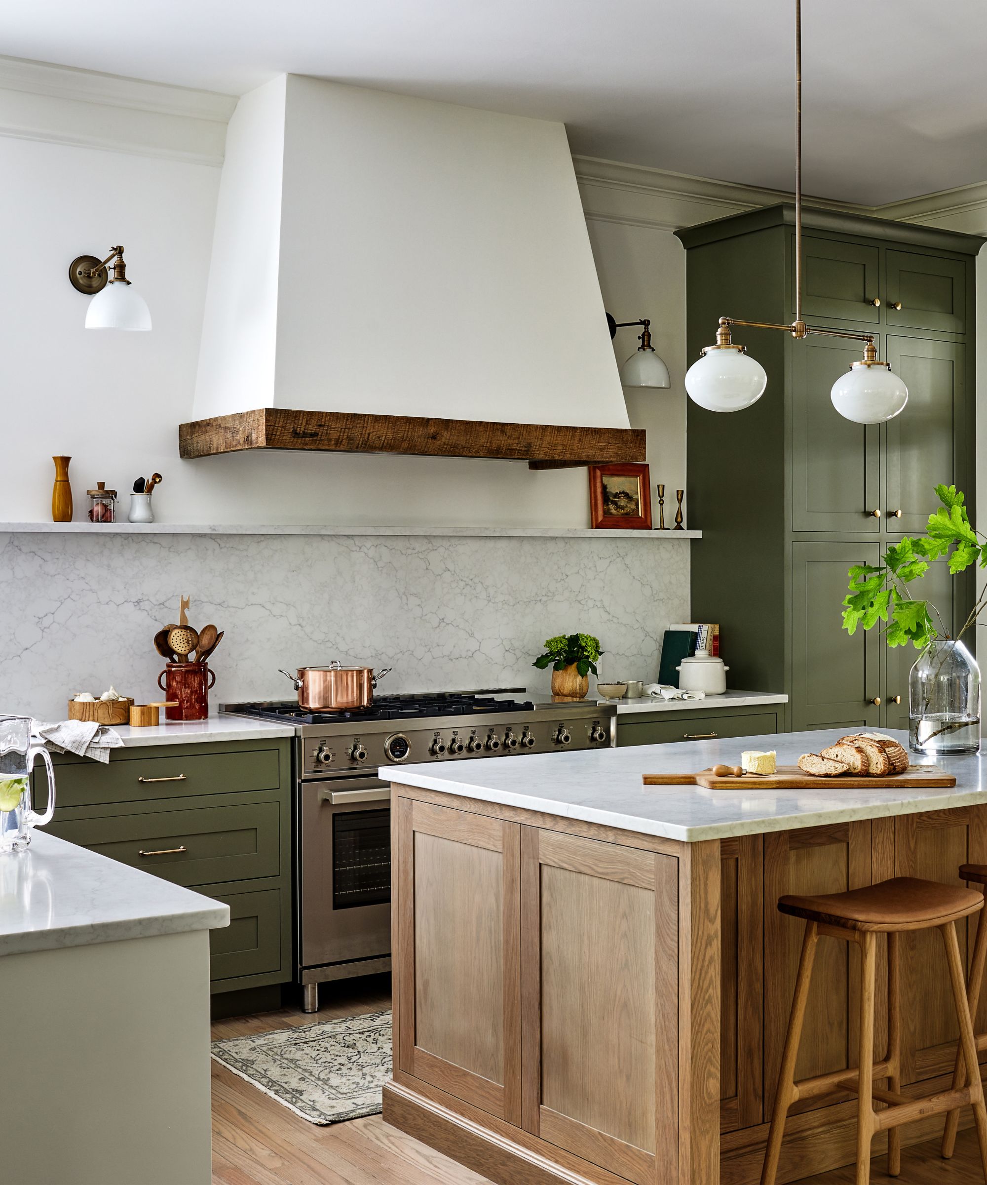 Bright kitchen with olive green cabinets, a large white range hood with rustic wood trim, marble countertops, and a wooden island with barstools.