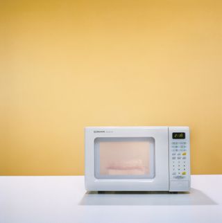 A white microwave sat on top of a white surface against a yellow wall.