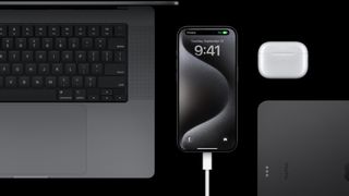 iPhone 15 Pro charging next to a Macbook, airpods, and an iPad