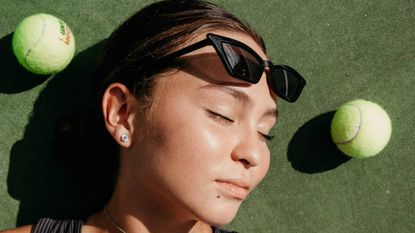 Woman with sunglasses on her head lying down with tennis balls around her