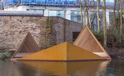 The floating platform placed on the river is constructed out of wood and is in the shape of three triangles that are connected.