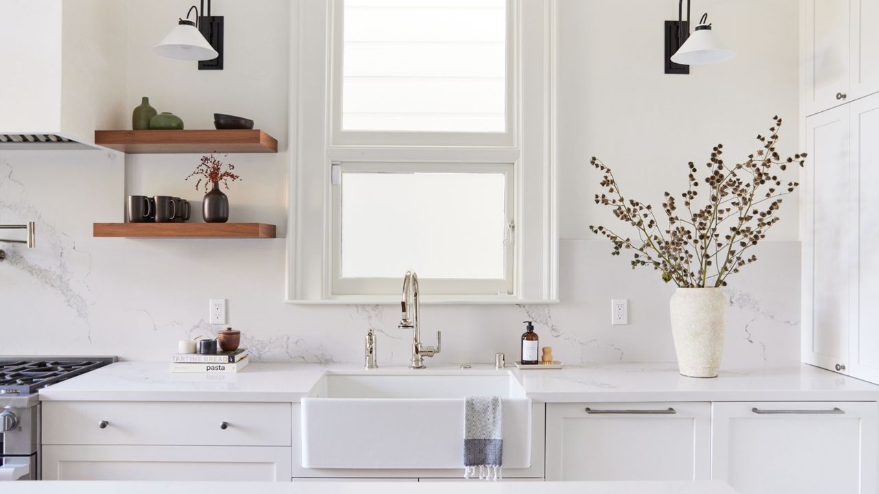 things that interior designers warn make a kitchen look cheap, white kitchen with marble countertop and backsplash, dark wood open shelving, Butler sink 