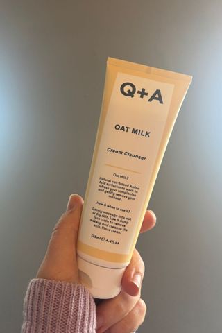 a hand holding a tube of Q+A oat milk cleanser