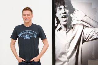 Musician and photographer Bryan Adams poses beside a portrait of Mick Jagger on display at his photography exhibition 'Hear The World Ambassadors' at Saatchi Gallery on July 21, 2009 in London, England. (Photo by Chris Jackson/Getty Images)