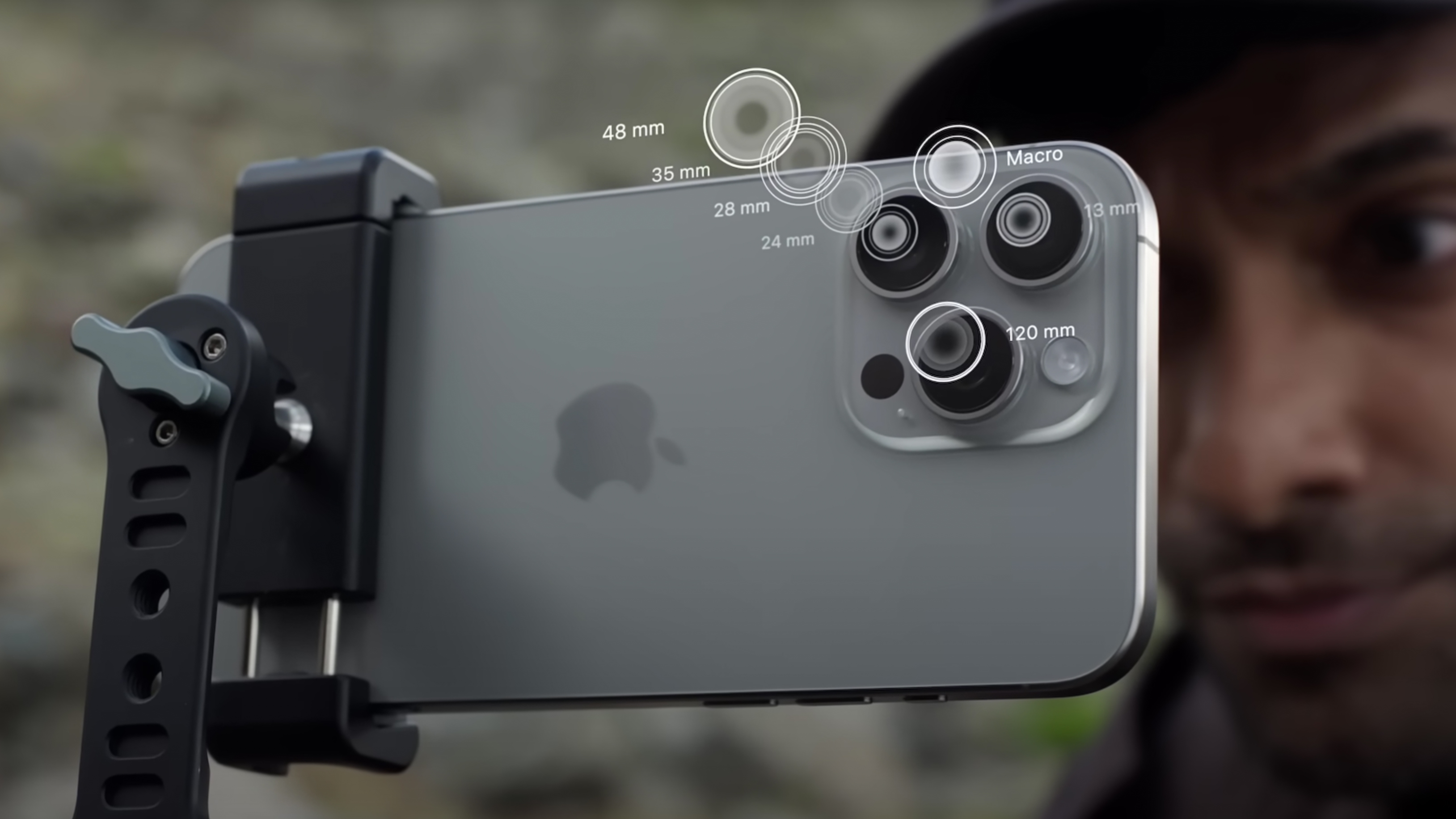 iPhone 15 Pro Max pada tripod dengan seorang pria melihat melalui layar