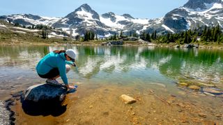 Woman filling water bottle from a mountain stream