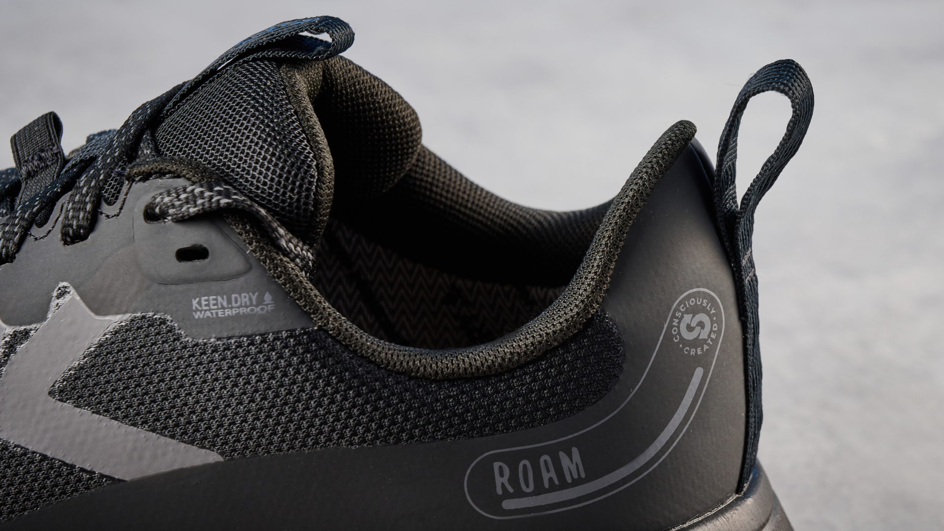 Keen Roam train running shoes in black photographed in front of a blue background