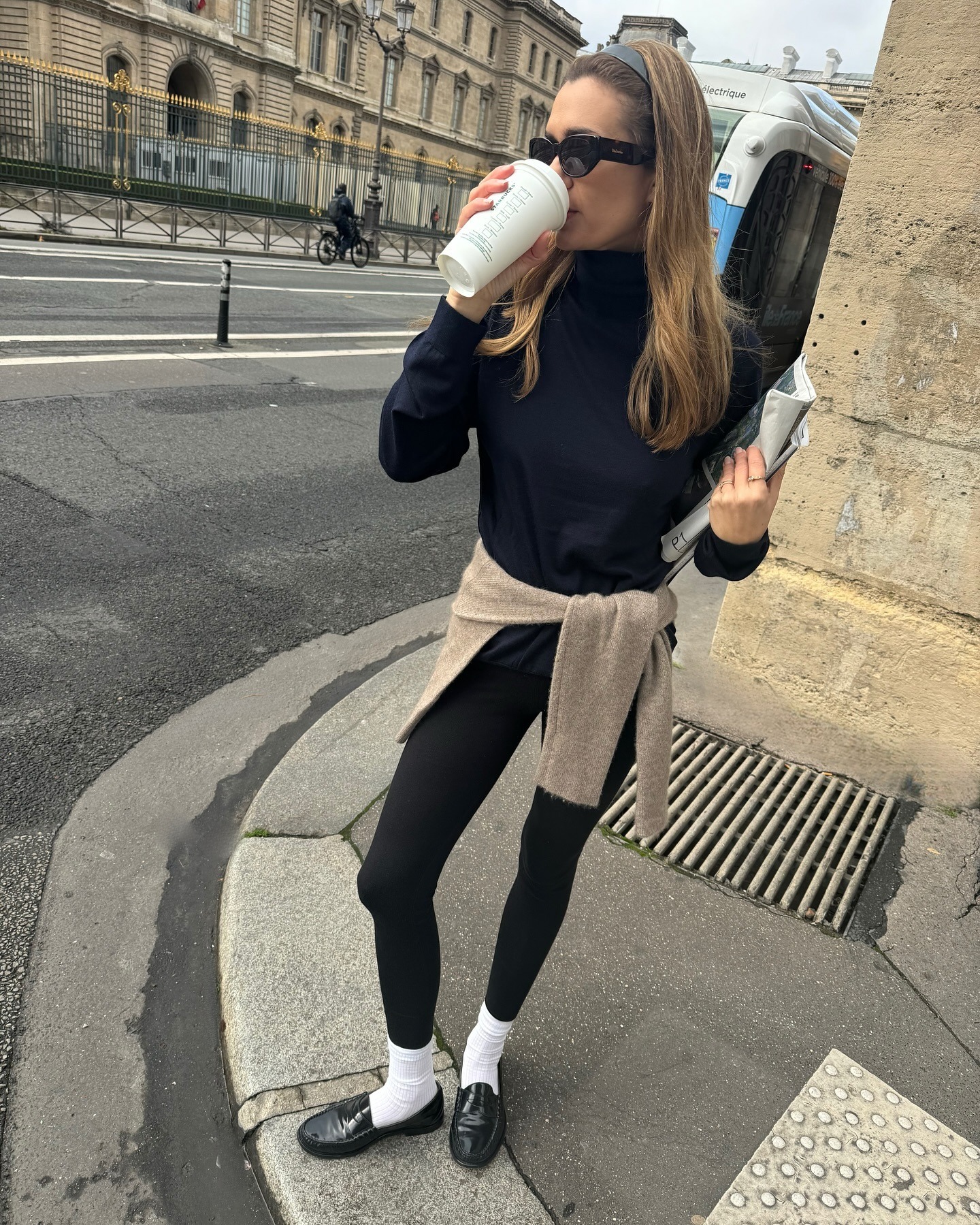 Fashion person Anne Laure Mais wears a leggings outfit 2025. She wears black leggings, a black jumper and a waisted tied taupe jumper.