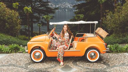 JJ Martin in an orange soft top car overlooking a lake in Italy