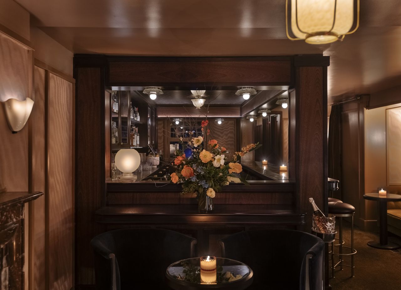 A sumptuously decorated bar features warm Art Deco lighting, refined cabinetry, and curtain-paneled walls.