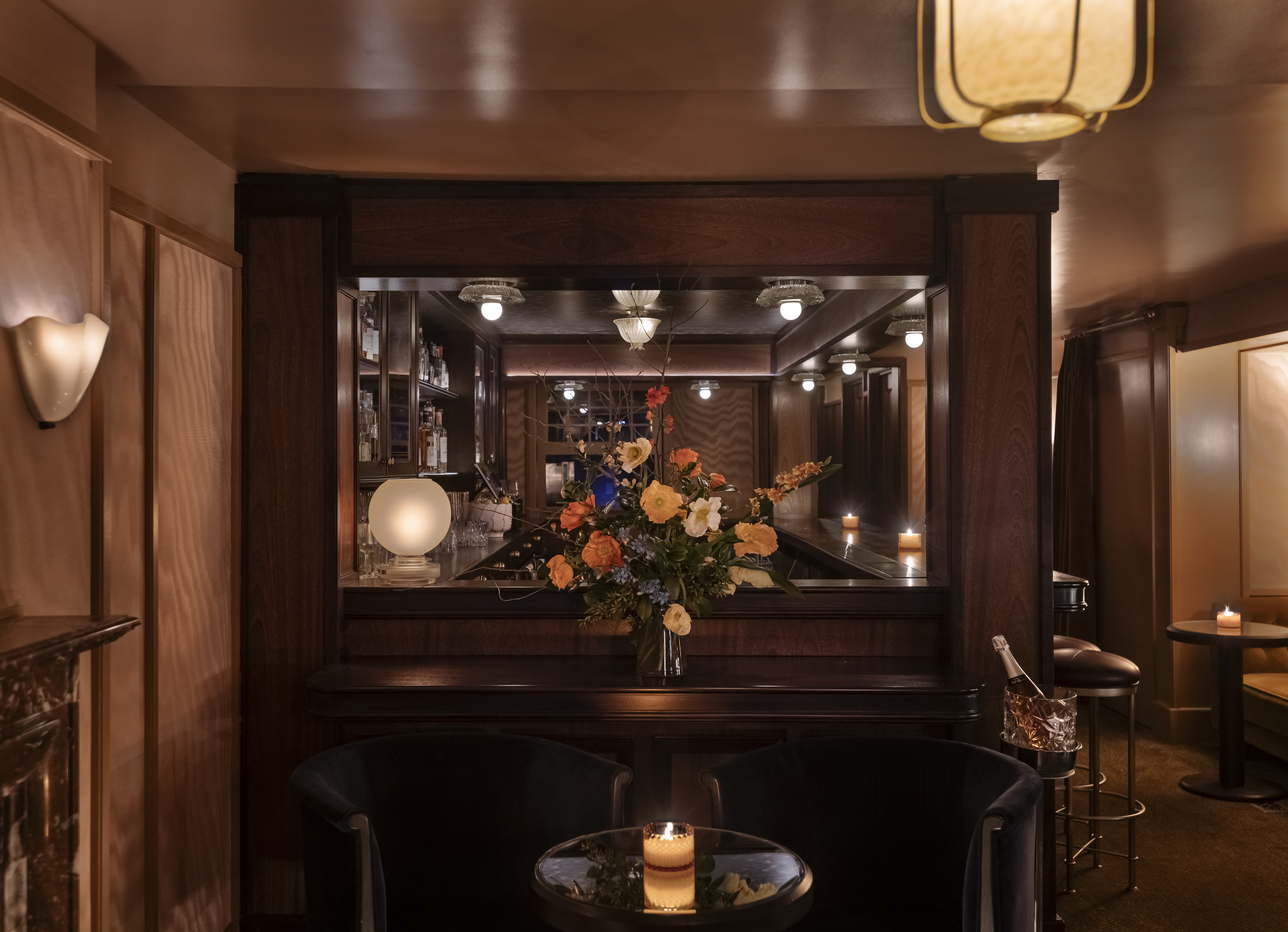 A sumptuously decorated bar features warm Art Deco lighting, refined cabinetry, and curtain-paneled walls.