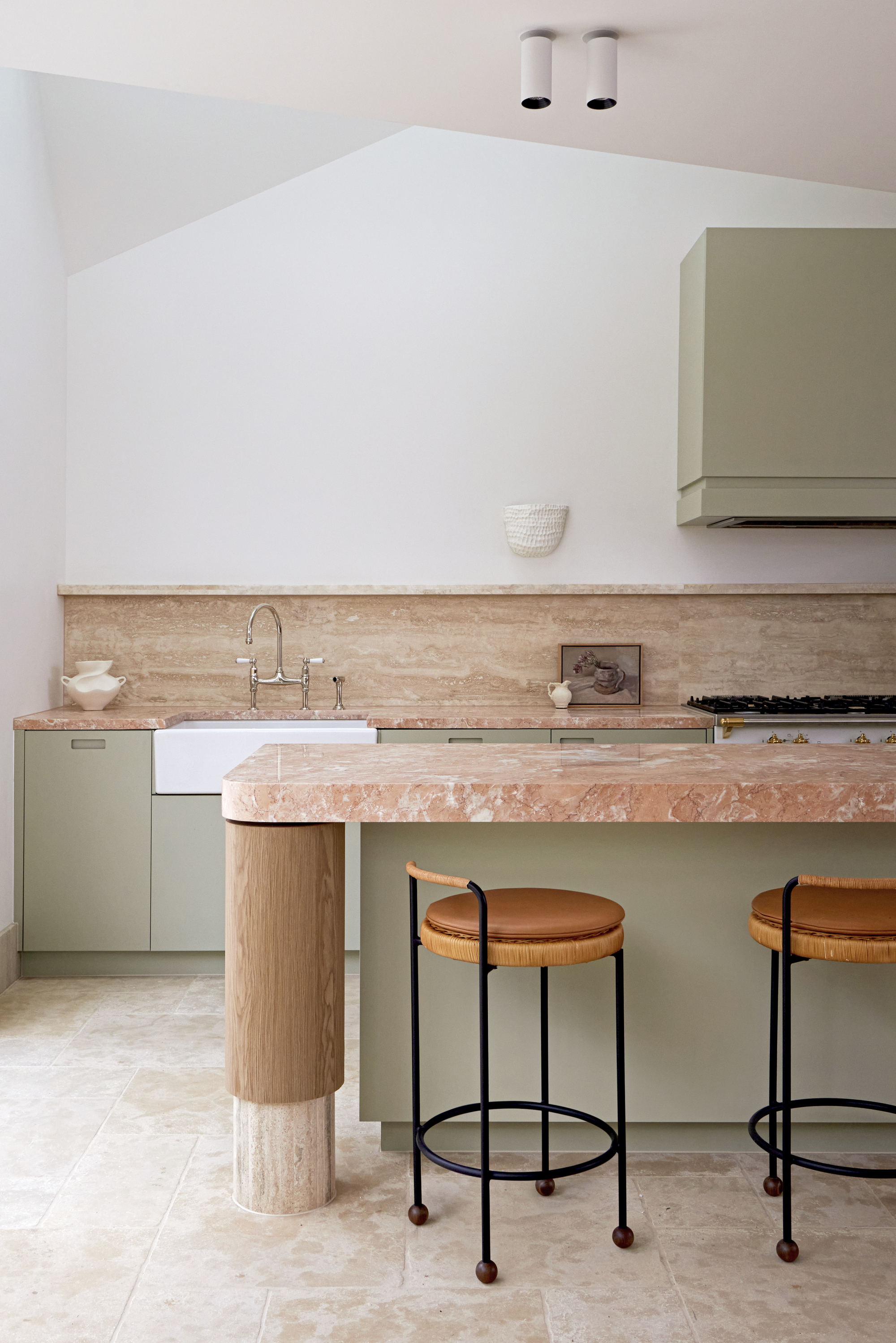 orange and green kitchen with orange stone countertops, light sage green cabinetry, stone floor, backsplash with display ledge, and bar stools with leather seats