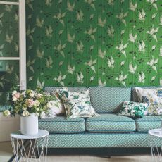 A living room with a wall covered in a green floral wallpaper and a printed sofa in front of it